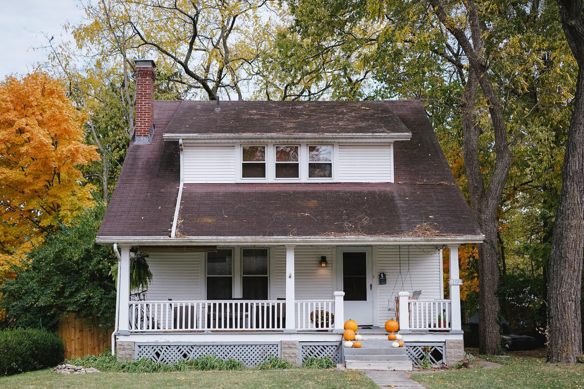 Maison entourée d'arbres avec feuilles tombant près des gouttières